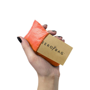 ZeroBag original, the reusable shopping bag made from upcycled parachutes. Super strong and orange in colour. Folds into a small pouch as seen here held in the palm of a hand.