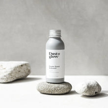 Dust & Glow powder body wash in a grey aluminium bottle sitting on a stone.