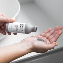 Dust & Glow powder based detox cleanser and facemask being dispensed into an outstretched hand next to a bathroom sink.