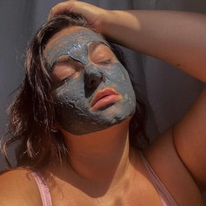A lady with closed eyes wears a string vest and leans her head back in the sun, visibly relaxing as she wears Dust & Glow's detox facemask.
