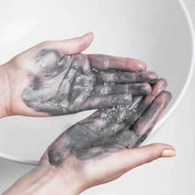 Dust & Glow powder based detox cleanser and facemask being used on outstretched hands which are covered in dark grey creamy cleanser over a bathroom sink.