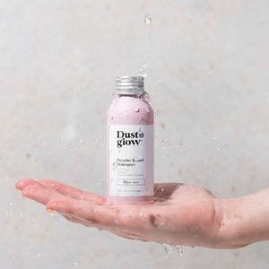 Dust & Glow powder based shampoo in a recyclable aluminium bottle on an outstretched hand with water droplets falling on it from above.