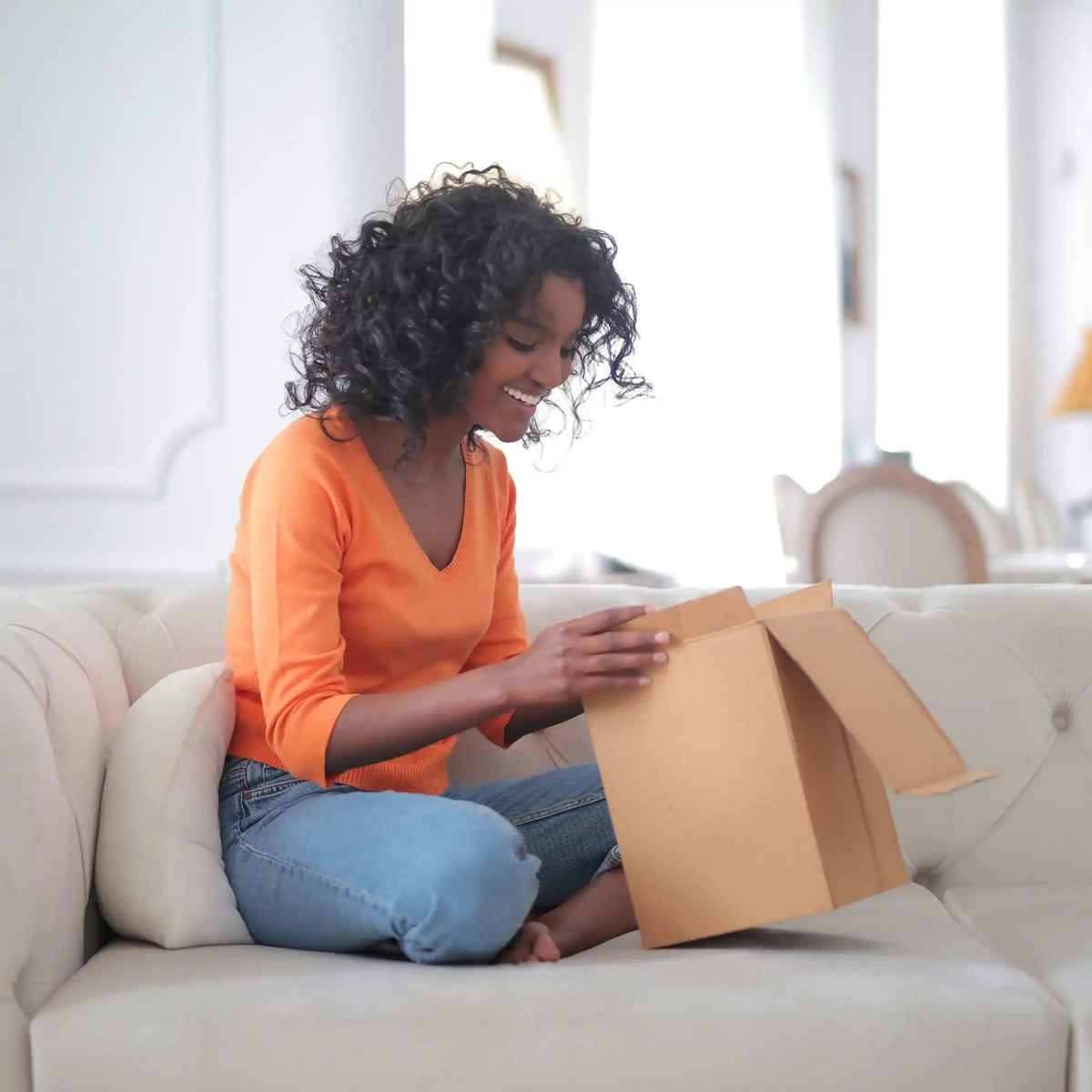 Image of woman sitting on couch opening a cardboard box depicting that Earthlove packaging is recycled, compostable and environmentally friendly.