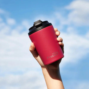 Made by Fressko insulated stainless steel coffee cup in red / rouge colour raised high with a blue cloudy sky background