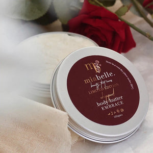 Mia Belle rich Embrace whipped body butter in an aluminium tin in a soft setting with red roses in the background and soft linens in the foreground.
