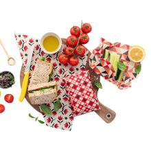 Nil products vegan food wrap in the red pōhutukawa design pictured on a wooden chopping board under a sandwich and surrounded by other fresh food.