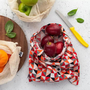 Organic cotton produce bags containing fruit on a benchtop. Bags are red, white and natural in colour. 