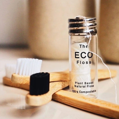Plant based compostable dental floss in a glass jar with bamboo toothbrushes in the foreground.