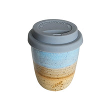 An espresso sized ceramic travel take-away coffee keep cup by Wellhandled Ceramics inspired by the beach with a layered glaze that gives the feel of sand (speckled buff clay), surf (white glaze layer) and sea (light blue glaze layer) and a grey coloured silicone lid.