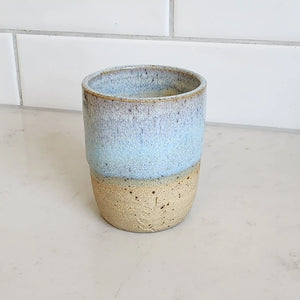 Ceramic espresso sized drinking tumbler handmade by Wellhandled Ceramics with a beachy coloured clay and a light sea foam glaze. Pictured on a light coloured kitchen bench.