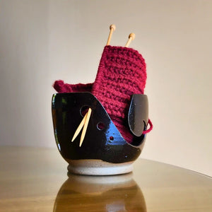 Ceramic yarn / wool bowl to hold your knitting or crochet project. A hand carved koru swirling shape on the side allows space to feed your yarn through and 3 holes on the side keep your needles safe when not in use. Hand thrown in Christchurch and glazed with a silky black, slightly specked glaze. Seen here with red yarn and bamboo knitting needles.
