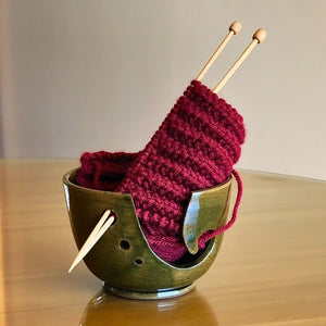 Ceramic yarn / wool bowl to hold your knitting or crochet project. A hand carved koru swirling shape on the side allows space to feed your yarn through and 3 holes on the side keep your needles safe when not in use. Hand thrown in Christchurch and glazed with a silky forest green, slightly specked glaze. Seen here with red yarn and bamboo knitting needles.