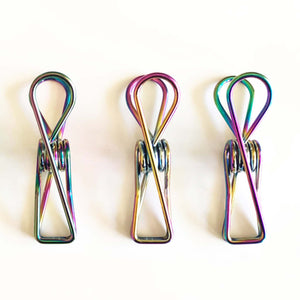 Close up of 3 stainless steel clothes pegs in rainbow colour.