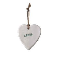 White ceramic hanging heart with a jute string and stamped with Aroha meaning love. The letters are a beautiful dark green.