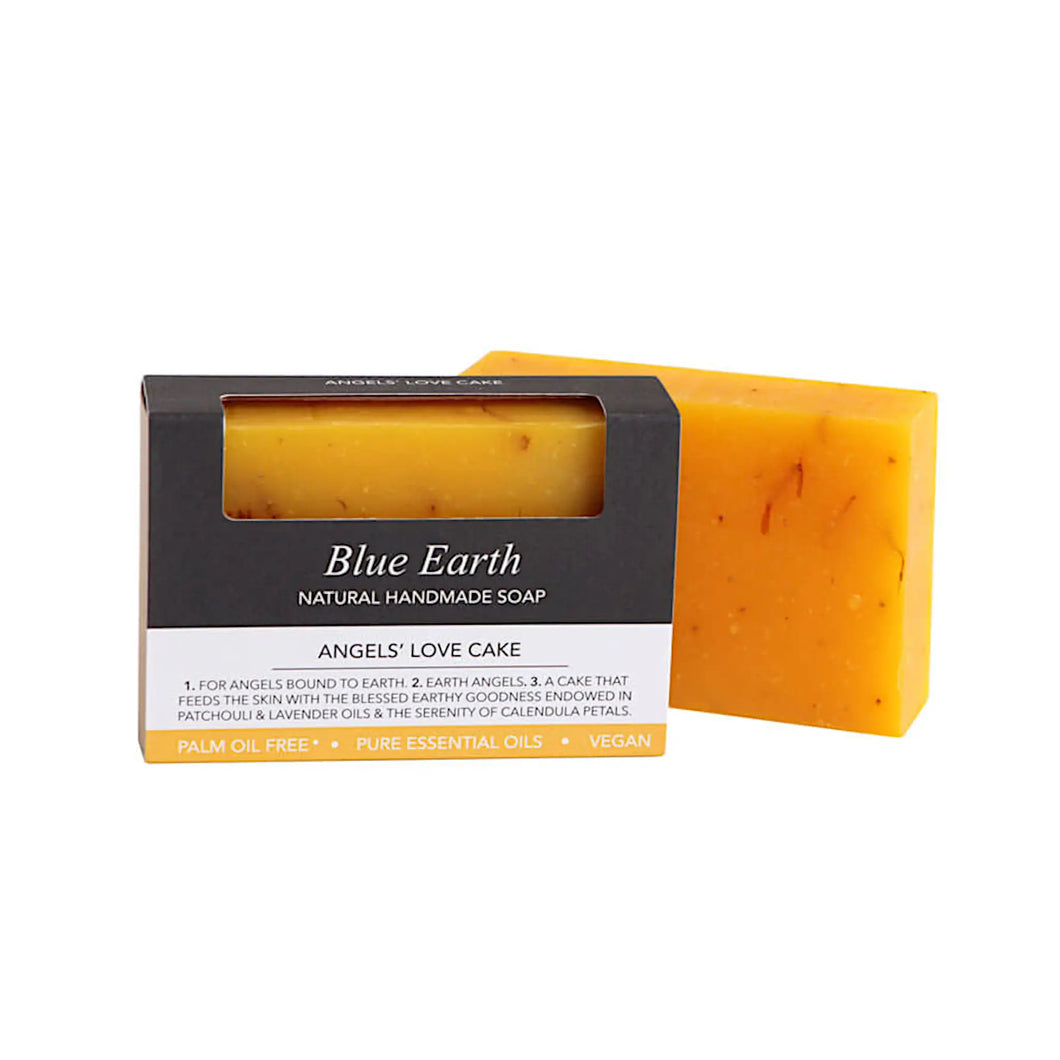 Blue Earth's Angel's Love Cake soap bar, natural handmade soap pictured with one bar packaged and one bar standing to the right and slightly behind the packaging. The soap bar is brighly coloured with yellow / orange calendula petals. The soap box has an open window which allows one to see and smell the soap. Packaging reads: Natural Handmade soap, for angels bound to Earth. A soap that feeds the skin with patchouli and lavender oils and soothes with calendula petals.