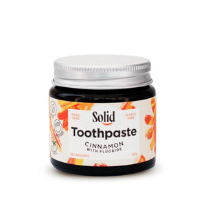 Solid Oral Care cinnamon flavoured toothpaste with fluoride in an amber glass jar and aluminium lid. The white label with light dark orange swirls reads made in NZ and plastic free.