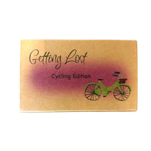Cycling edition of the Getting Lost Adventure game in a kraft cardboard box with a purple cloud and a green bicycle with a brown basket  on the front.