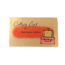 The Everybody edition of the Getting Lost Adventure game in a kraft cardboard box with an orange cloud and a stack of two vintage suitcases on the front.