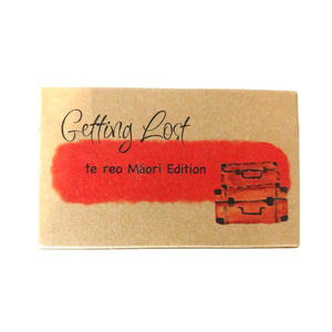 Te reo Māori edition of the Getting Lost Adventure game in a kraft cardboard box with an orange cloud and a stack of two vintage suitcases on the front.
