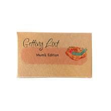 Mum's edition of the Getting Lost Adventure game in a kraft cardboard box with a light pink cloud and a straw hat on the front with a blue ribbon and flowers.