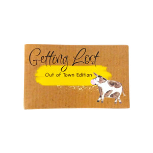 Out of Town edition of the Getting Lost Adventure game in a kraft cardboard box with a yellow cloud and a cow on the front.