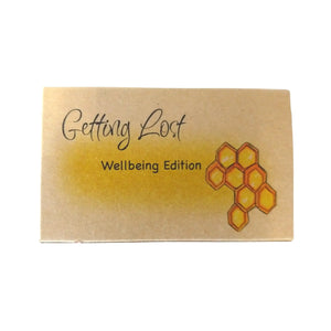 The Wellbeing edition of the Getting Lost Adventure game in a kraft cardboard box with a yellow cloud and a yellow and orange honeycomb on the front.