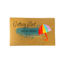 Winter edition of the Getting Lost Adventure game in a kraft cardboard box with a blue cloud and a multi coloured umbrella on the front.
