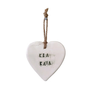 Beautiful white hanging heart embossed with the letters "Kia Kaha" meaning stay strong in te reo Māori. The letters are a very dark, almost black green. A jute string is attached to a hole in the top of the heart to hang your heart up by.