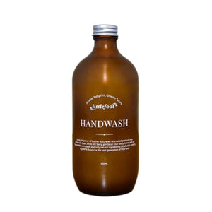 500ml amber glass bottle with aluminium screw-top lid containing hand wash liquid. The clear label with white text reads: smaller footprint, greener future, Littlefoot logo, and Handwash.