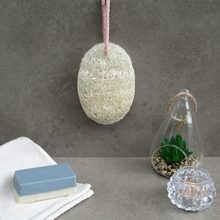 Loofah soap saver pocket hanging in a bathroom with soap and towel in the foreground.