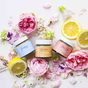 A trio of Little Mango natural and vegan deodorants surrounded by flowers and cut lemons.