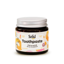 Solid Oral Care orange flavoured toothpaste with fluoride in an amber glass jar and aluminium lid. The white label with orange swirls reads made in NZ and plastic free.