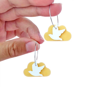 Eco friendly Flocking Bird Gull earrings made from recycled ice-cream container lids in Ōtautahi Christchurch by Remix Plastic. Hypoallergenic hoops which are silver in colour and a golden cloud with a white silhouette bird in front. Seen here being held by fingers.