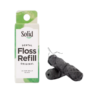 Black dental floss refill by Solid Oral Care. Two black floss refills lay beside the white and green cardboard box which reads 2 x 30m rolls of black dental floss.