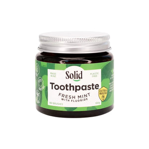 Solid Oral Care Fresh Mint flavoured toothpaste with extra protection fluoride in an amber glass jar with silver coloured aluminium lid. The green coloured label with white section in the middle reads made in NZ and plastic free.