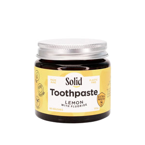 Solid Oral Care Lemon flavoured toothpaste with extra protection fluoride in an amber glass jar with silver coloured aluminium lid. The lemon coloured label with white section in the middle reads made in NZ and plastic free.