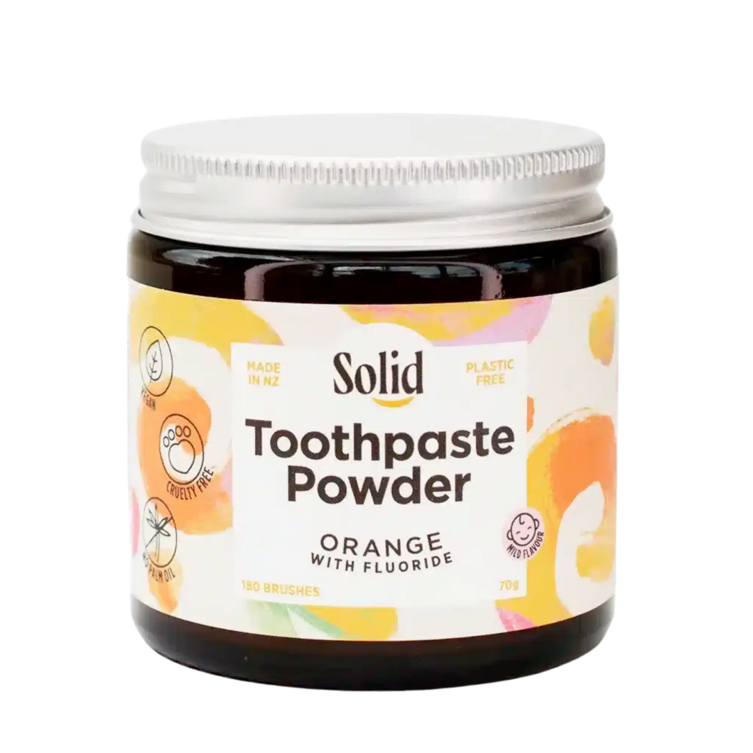 Amber glass jar with silver coloured aluminium lid containing Toothpaste Powder by Solid Oral Care. Label is white with orange swirls and reads Made in NZ, Plastic Free, Orange flavour with fluoride, 180 Brushes, Cruelty Free, Vegan and No Palm Oil.