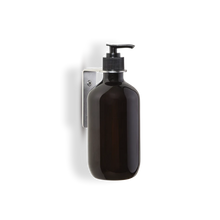 Amber glass bottle with pump dispenser being held in place with a 304 brushed stainless steel bottle holder which is attached to the bottle under the pump, hold bottle and remove pump to detach bottle from holder, can be screwed or taped into showers or anywhere you need a handy liquid dispenser.