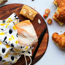 Organic reusable bread bag in yello flower design on benchtop with bread and food.