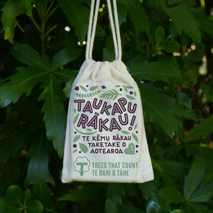 Tree Snap New Zealand's Native Tree Game, now available in te reo Māori - Taukapu Rākau! Te kēmu rākau taketake o Aotearoa, beautiful cards in a cotton drawstring bag hanging in front of dark green leaves.