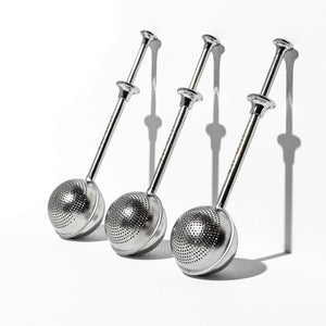 Three stainless steel loose leaf tea infusers leaning against a while wall.