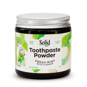 Amber glass jar with aluminium lid containing Toothpaste Powder by Solid Oral Care. Label is white with green swirls and reads Made in NZ, Plastic Free, Fresh Mint with Fluoride, 180 Brushes, Cruelty Free, Vegan and No Palm Oil.