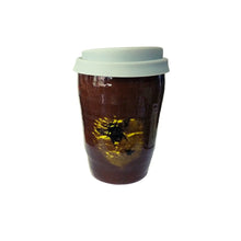 A ceramic large latte sized travel coffee cup in a glossy brown colour with a black image of a bee with yellow highlights and a grey silicone lid.